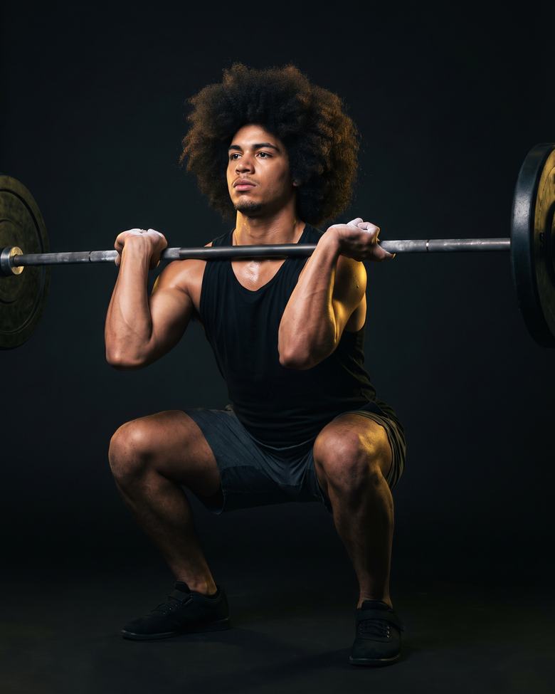 A man with a large natural afro at the bottom of a front squat.