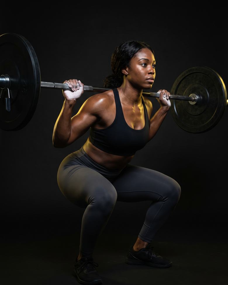 A woman at the bottom of a heavy barbell back squat, lit from one side against darkness.