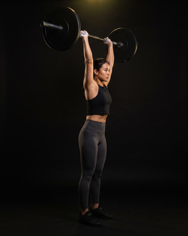 A woman holding a barbell locked out overhead.